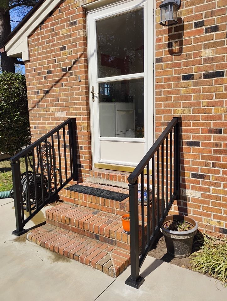 Brick house entryway with two black metal handrails flanking three brick steps leading to a white storm door.