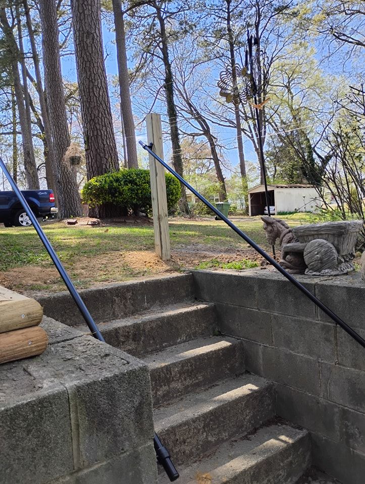 Two black metal railings are installed along stone steps leading to a yard with trees and a shed in the background.