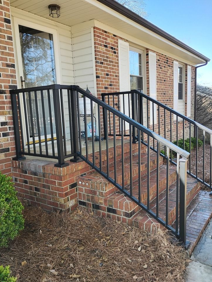Brick steps leading to a front door with black metal railings on both sides against a brick-and-siding exterior wall.