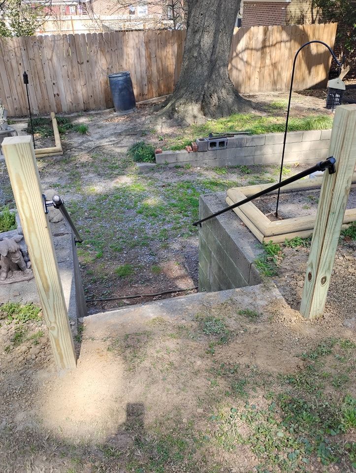 Outdoor stone stairs in a backyard with wooden support posts and two black metal handrails leading to a lower level.