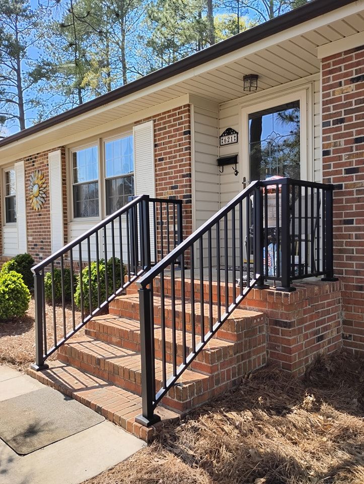 A brick front entrance of a house with black metal railings leading up three steps to a glass-paneled front door.
