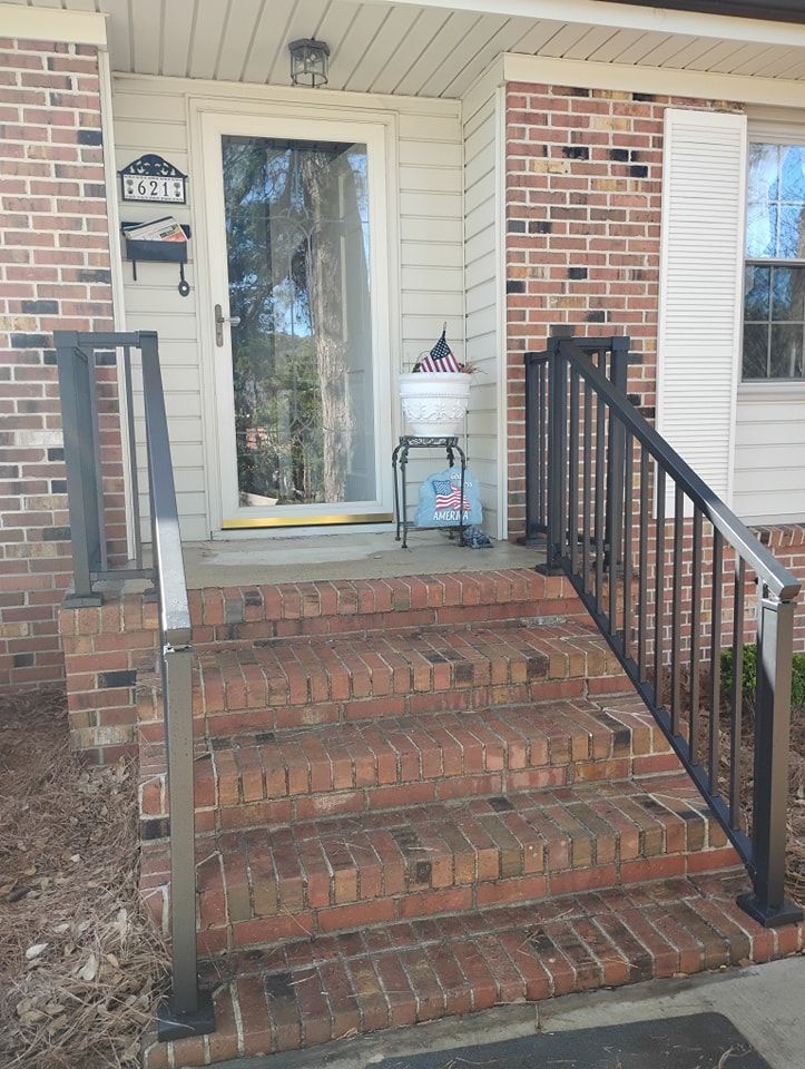 Brick steps leading to a front door with black metal railings on either side and a potted plant on a stand.