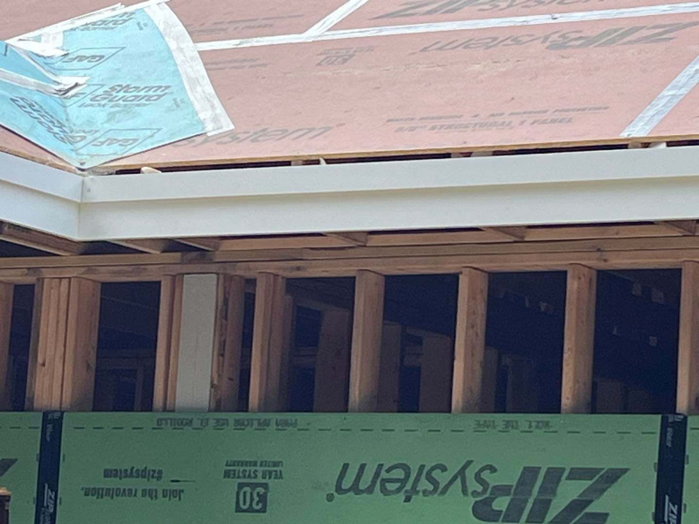 A close-up view of the exterior framing of a house under construction, showing wooden wall studs and roof sheathing.