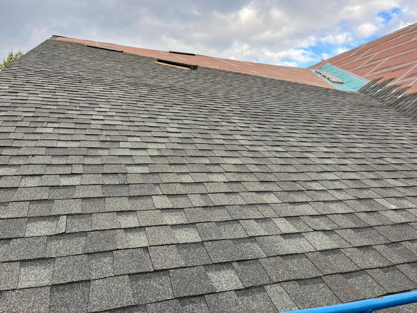 A sloped residential roof partially covered with new grey shingles and an unfinished section with red underlayment.