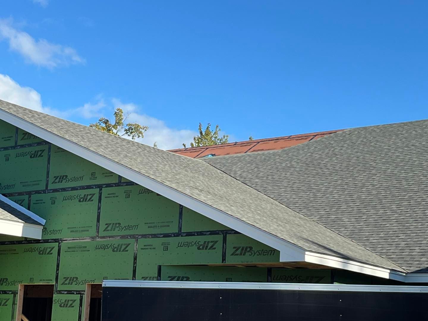A house under construction with green exterior wall panels and shingled roofing under a clear blue sky.
