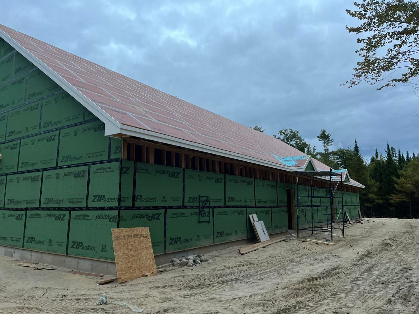 A building under construction featuring green exterior wall panels, a metal roof, and a gravel foreground.