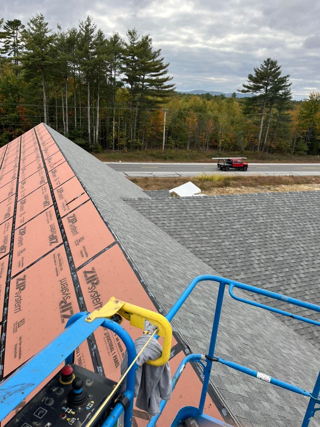 View from a lift of a roof under construction with ZIP System sheathing, shingles, and a road with a truck in the distance.