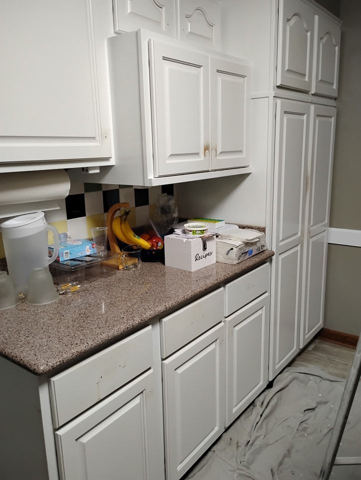 A kitchen corner featuring white cabinets, a speckled brown countertop with various items, and a checkered backsplash.