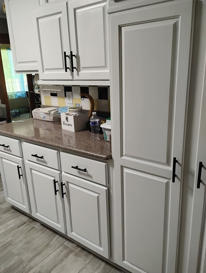 A kitchen view featuring white cabinets with black hardware, a brown countertop, and a tiled backsplash.