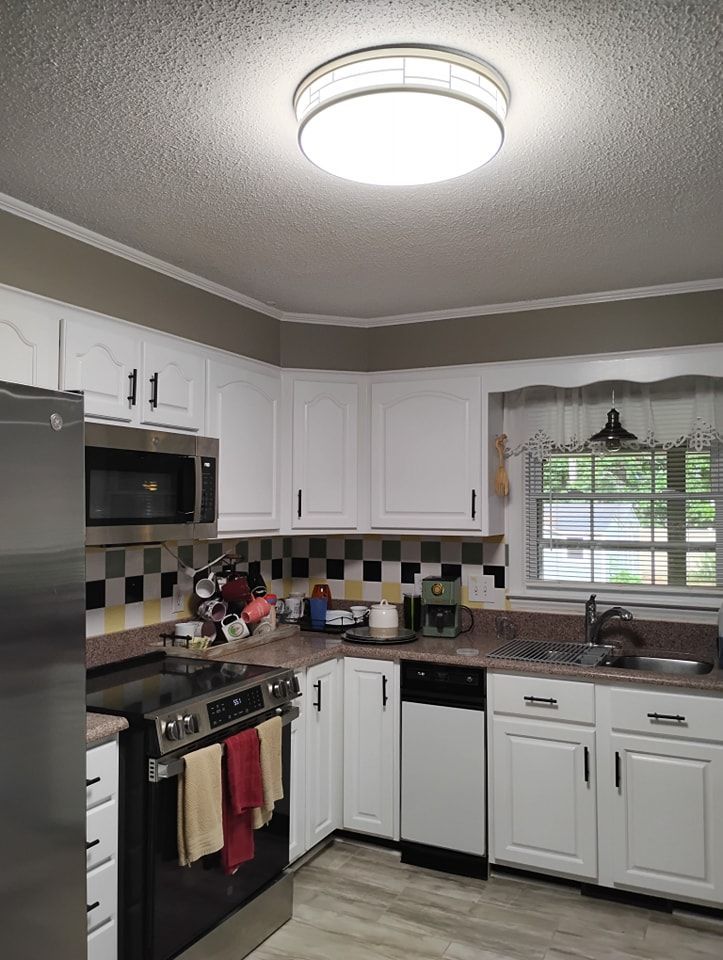 A white-cabinet kitchen with a stainless steel stove, microwave, checkered backsplash, and a central ceiling light.