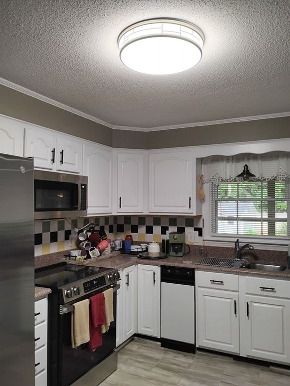 A modern kitchen featuring white cabinets, stainless steel appliances, a checkered backsplash, and a bright