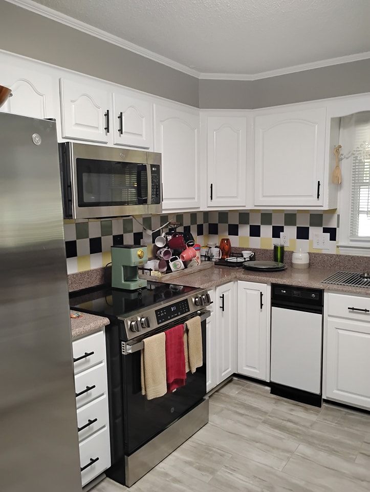 A brightly lit kitchen with white cabinets, stainless steel appliances, a checkerboard backsplash, and light wood flooring.