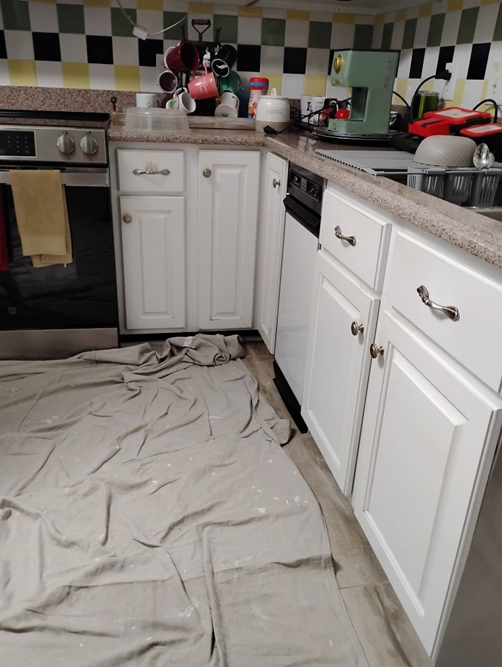 A white-cabinet kitchen with a checkered backsplash, featuring a stove, dishwasher, and a canvas drop cloth on the floor.
