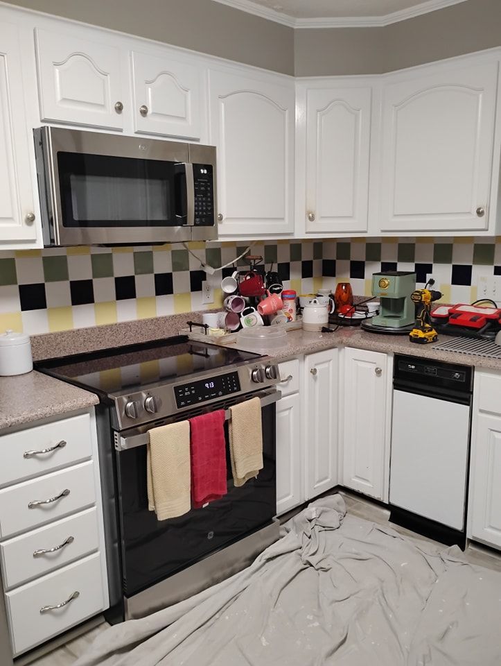 A kitchen with white cabinets, stainless steel appliances, and a checkerboard backsplash, with a drop cloth on the floor.
