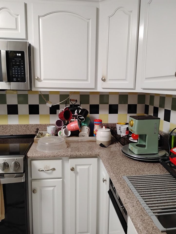 A kitchen corner featuring white cabinets, a black, yellow, and green tiled backsplash, and a light green coffee maker.