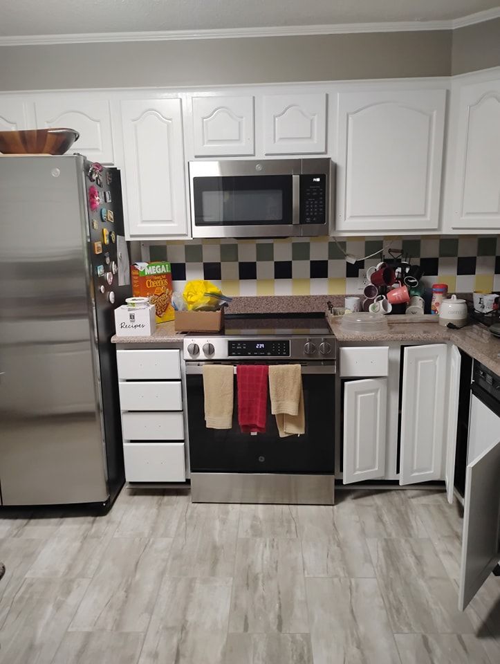 A kitchen with white cabinets, stainless steel appliances, a checkered backsplash, and light wood-look tile flooring.
