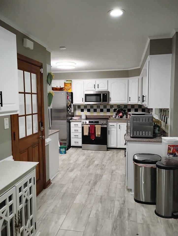 A kitchen with white cabinets, gray wood-look flooring, stainless steel appliances, and a wooden glass-paneled door.