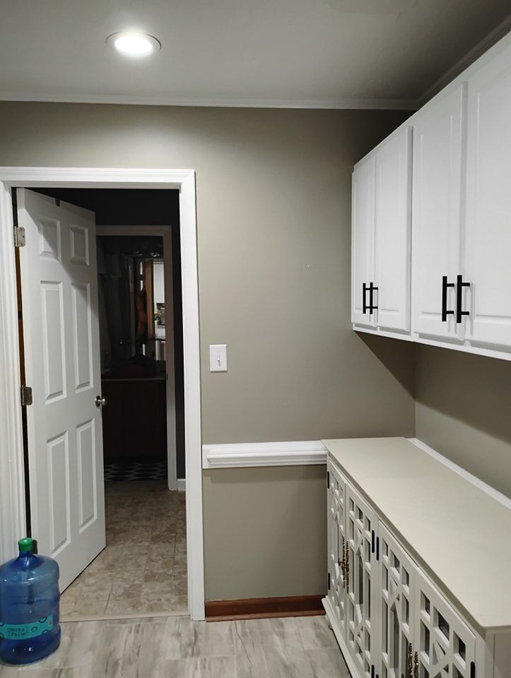 A neutral-toned room features white upper cabinets, a base cabinet with lattice doors, and a door leading to a hallway.