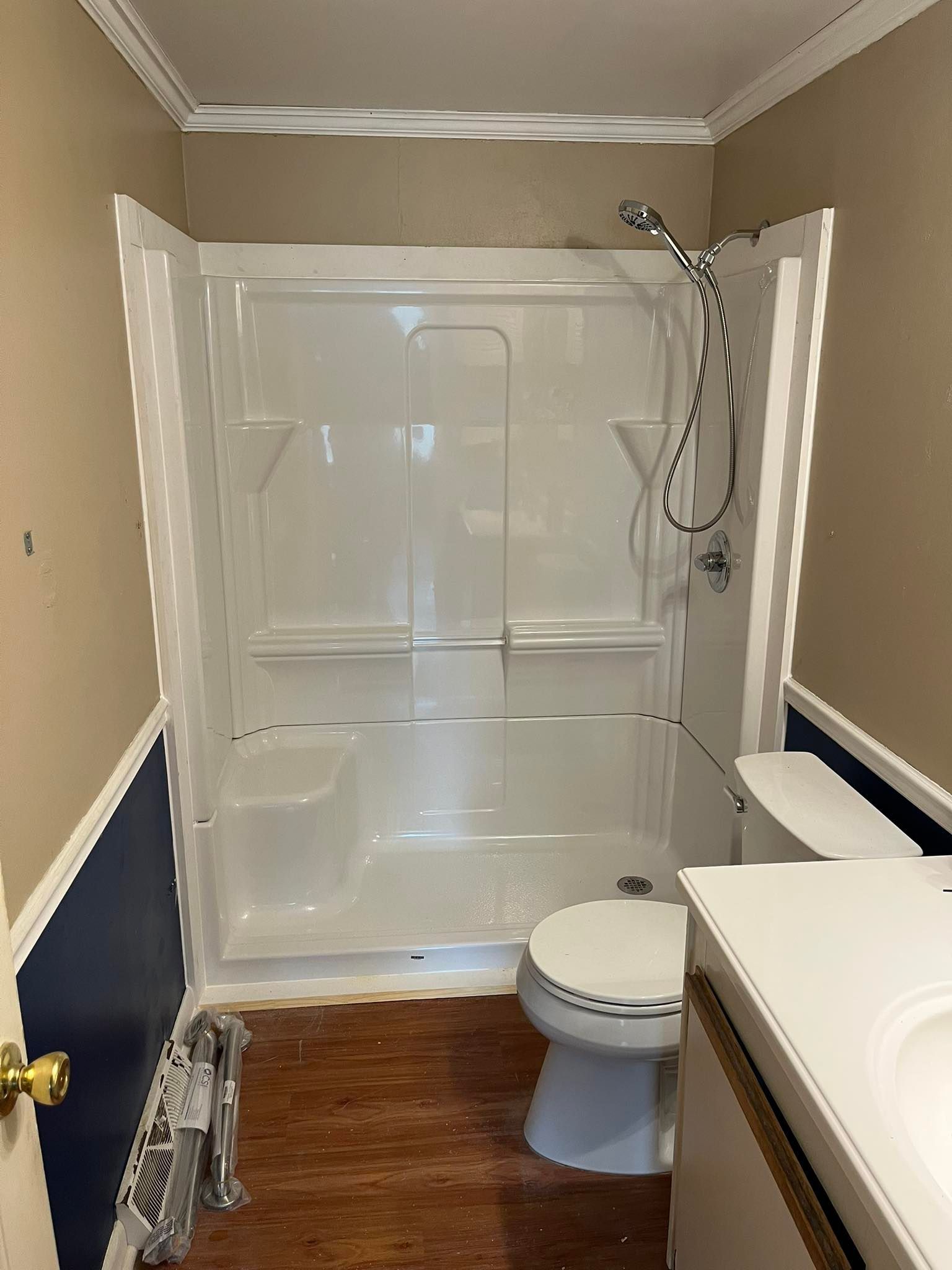 A small bathroom featuring a white shower stall, toilet, and vanity against beige and dark blue walls with wood flooring.