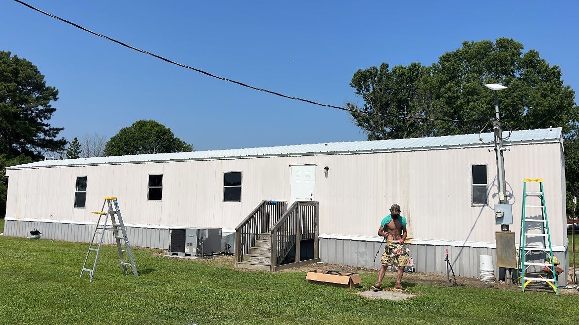 A person stands outside a mobile home with solar panels installed on the roof and a ladder positioned against the side.