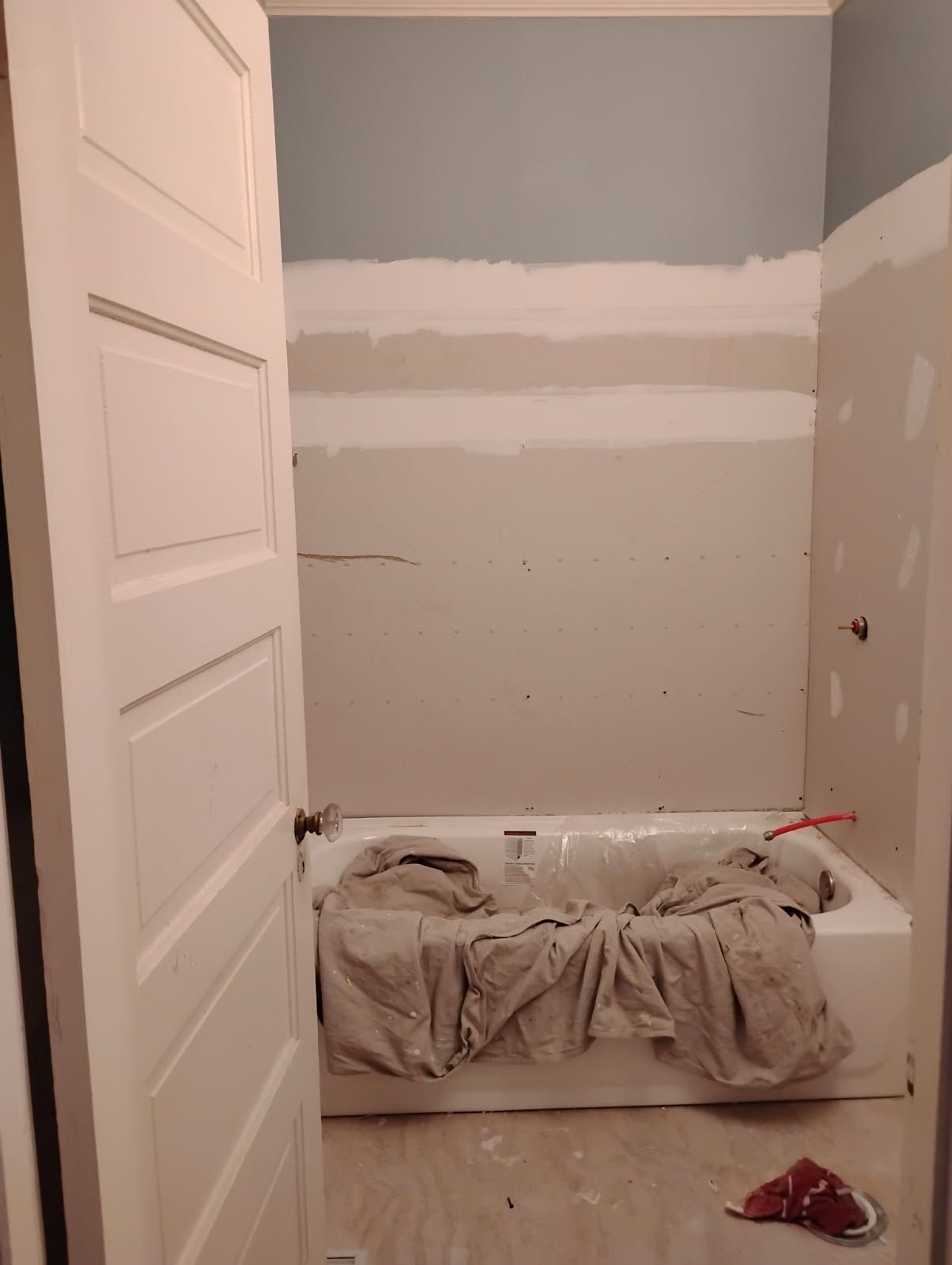 Bathroom under renovation with a partially painted wall and a bathtub covered in plastic sheeting.