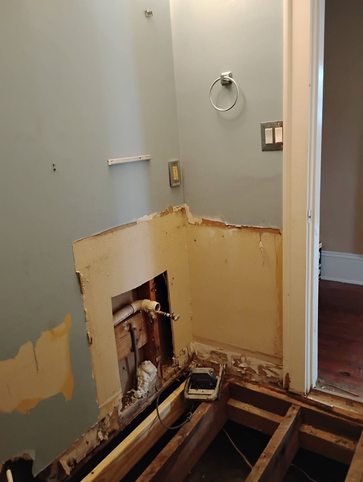 Bathroom wall and floor torn open for renovation, exposing plumbing and joists.