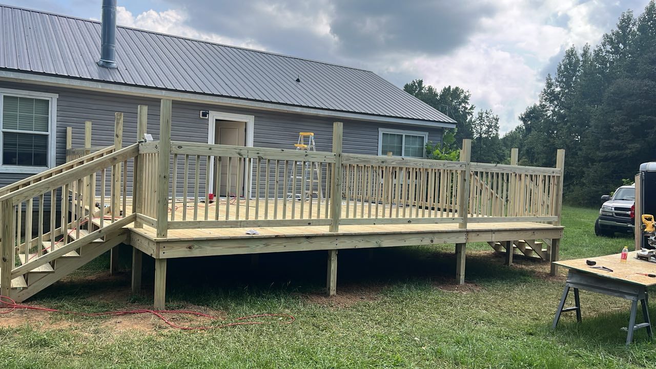 A newly constructed wooden deck with railings and stairs attached to the back of a house in a grassy yard.