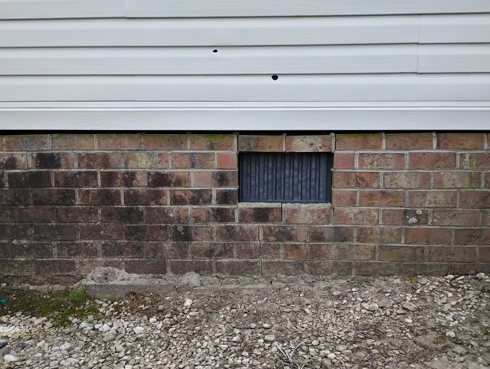 A crawl space vent set in a brick foundation wall beneath white horizontal siding.