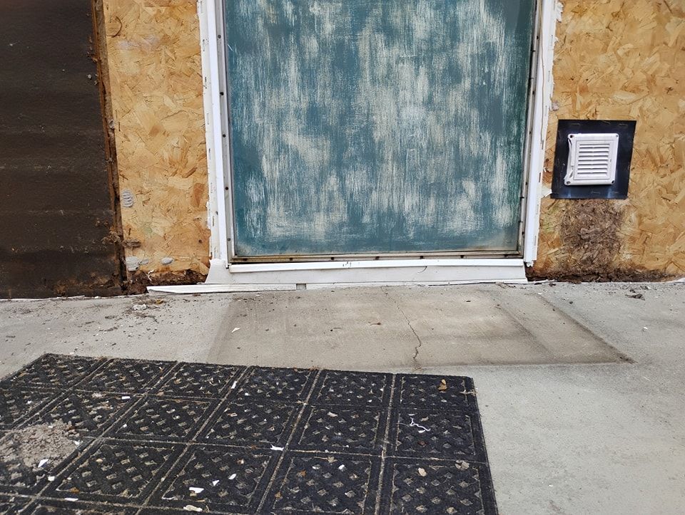 A close-up of a teal exterior door set in an unfinished OSB wall, with a small vent and a concrete threshold.