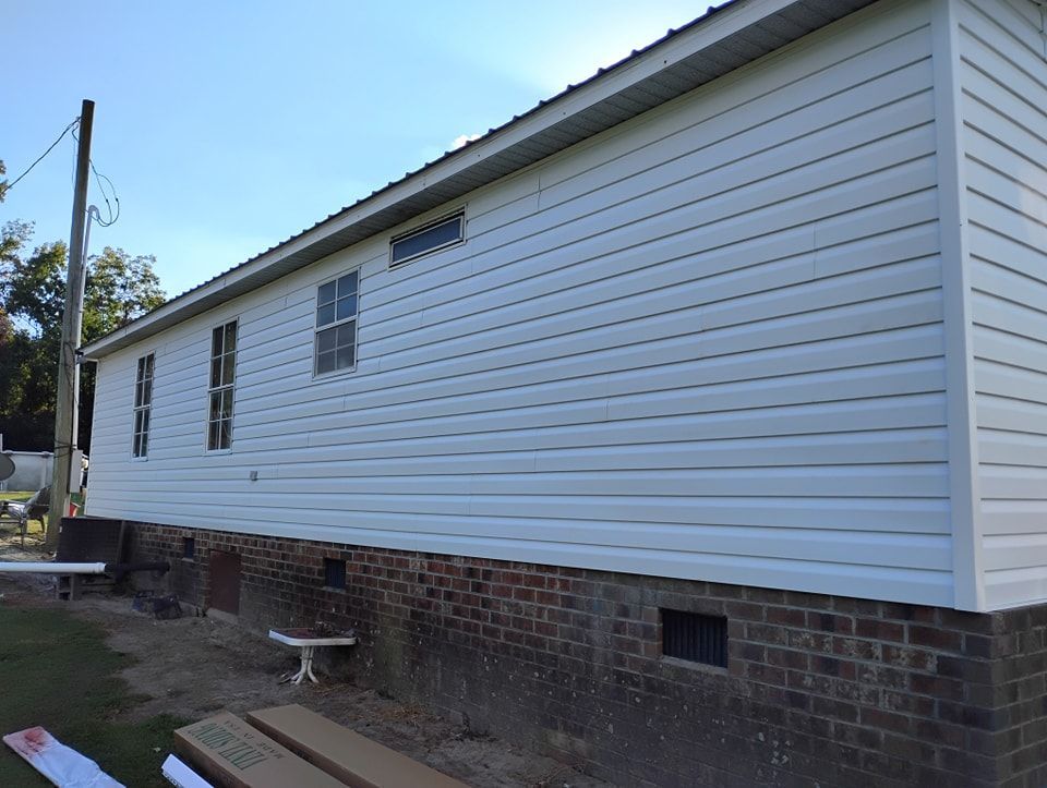 A side view of a house with white horizontal vinyl siding over a brick foundation, featuring three rectangular windows.