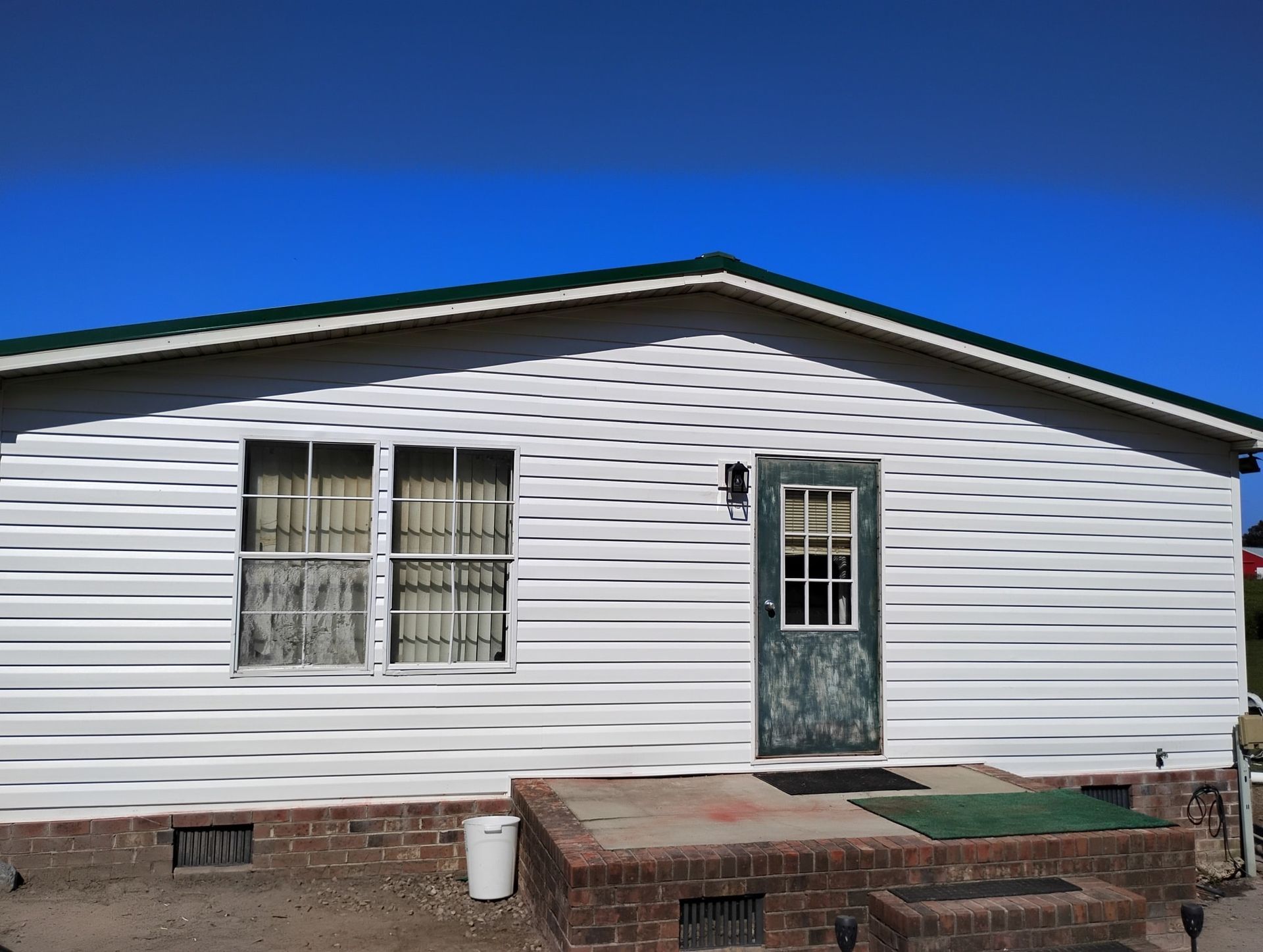 White single-story manufactured home with horizontal siding, a brick foundation, and a front entry door with a window.