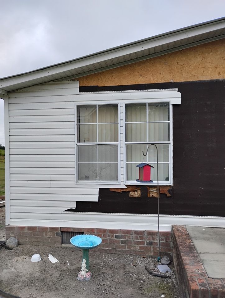 A house exterior with half-installed white horizontal siding over dark sheathing, partially framing a white window.