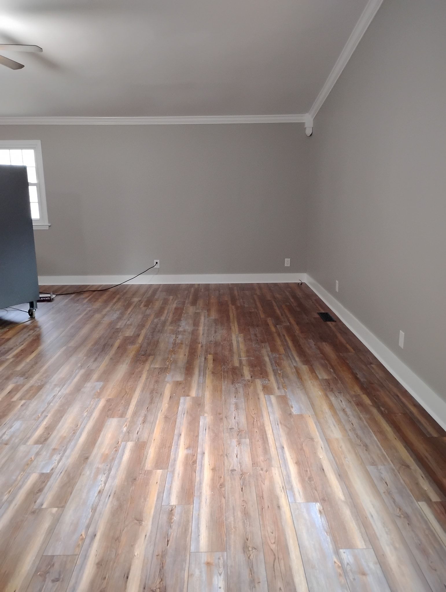 An empty room with light gray walls, white trim, and partially sanded or weathered wood-plank flooring.