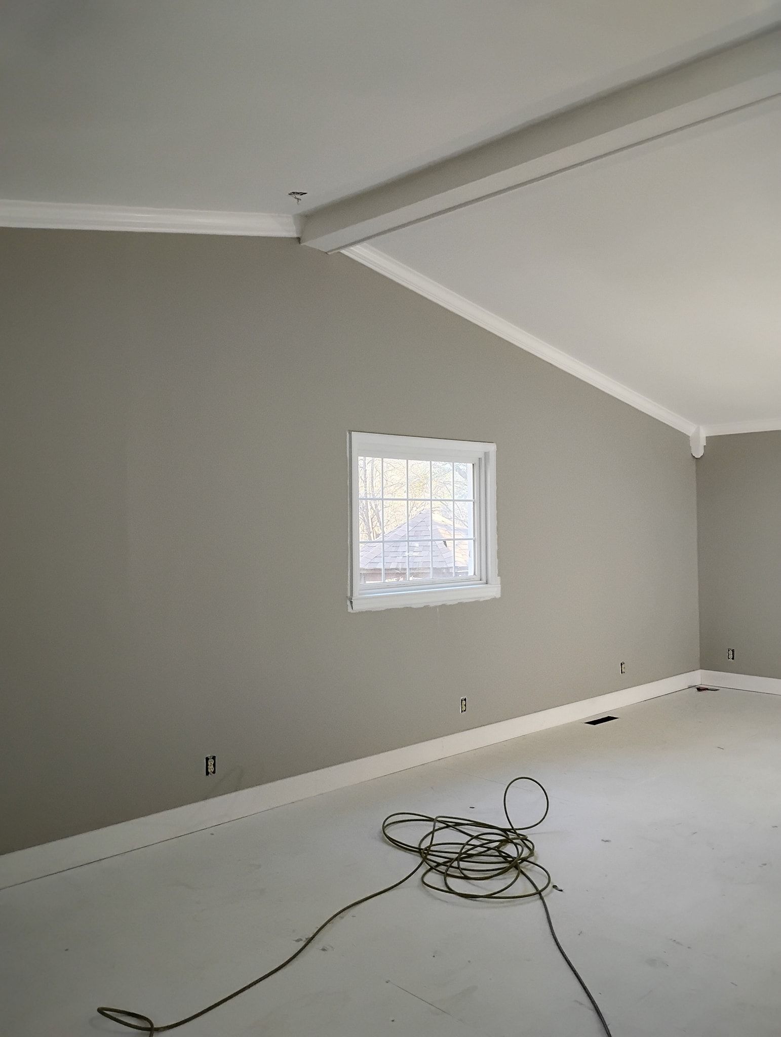 An interior view of a room under construction with gray walls, white trim, a single window, and a coiled electrical cord.
