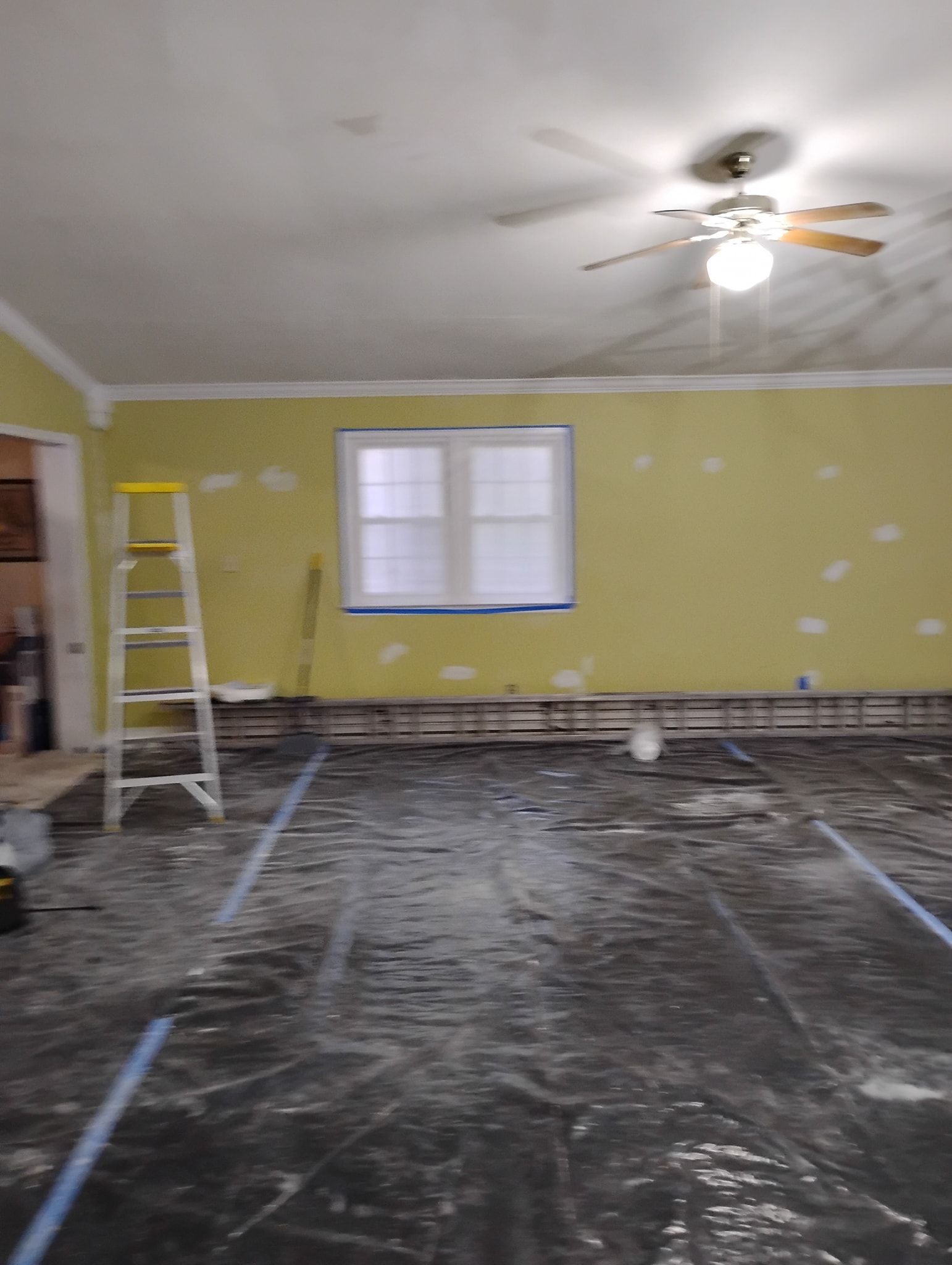 A room under renovation with yellow walls, a step ladder, and floor covered with protective plastic sheeting.