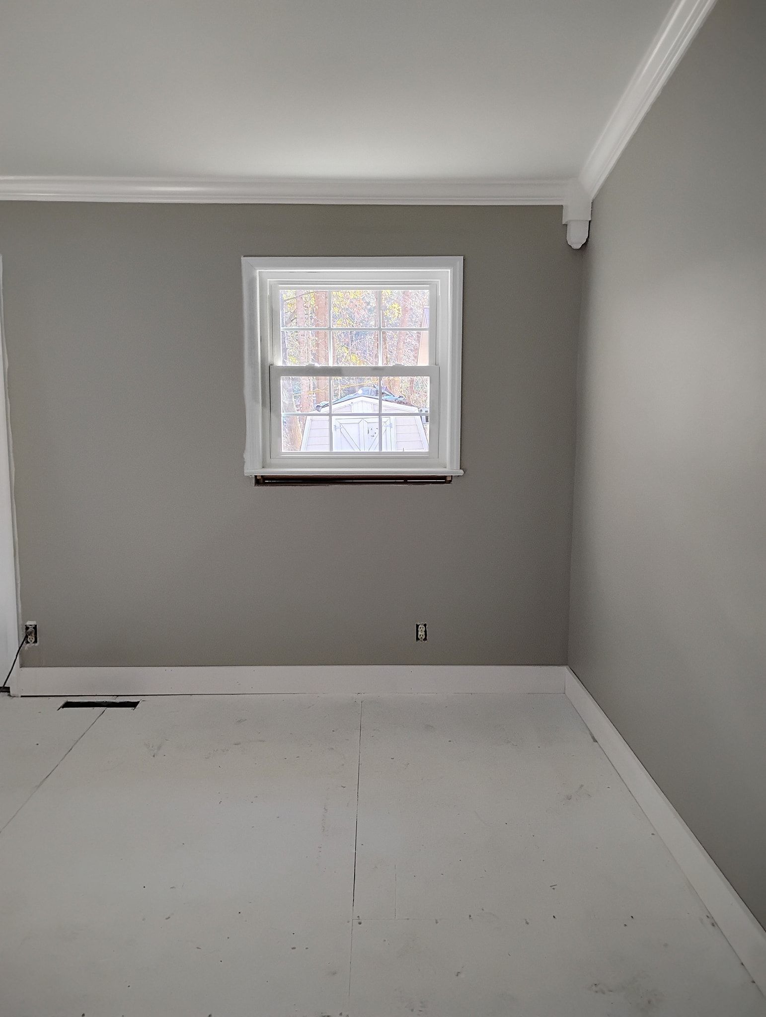 Empty room with gray walls, white trim, a single window, and unfinished subflooring.