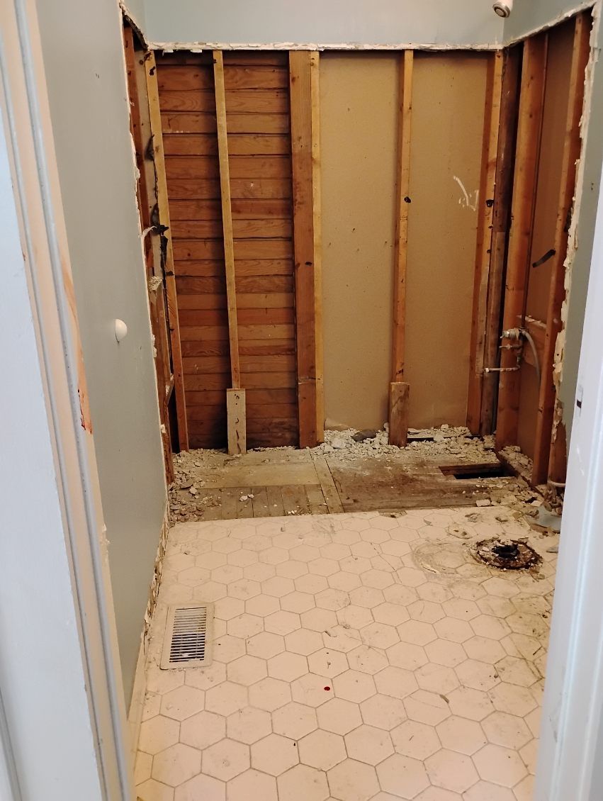 Partially demolished bathroom with exposed studs, debris, and hexagonal tile floor