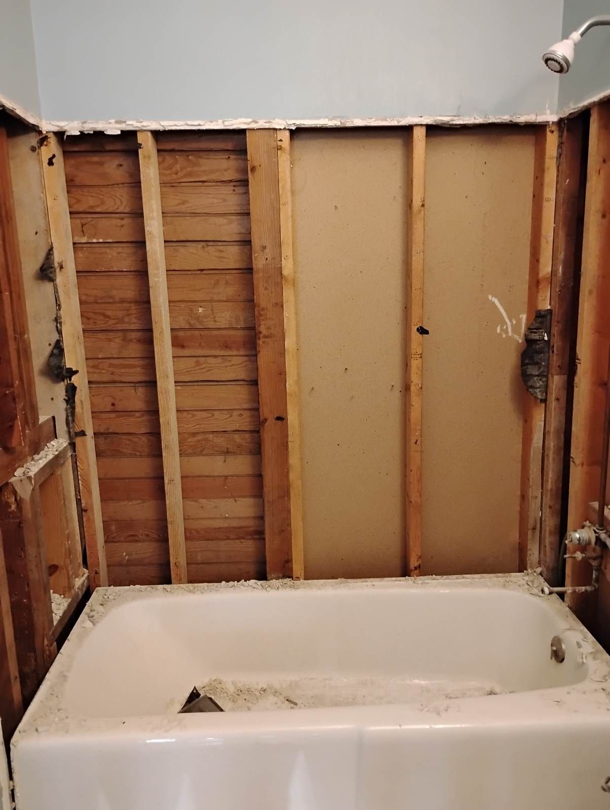 Partially demolished bathroom with exposed wall studs and a bathtub below the open wall cavity