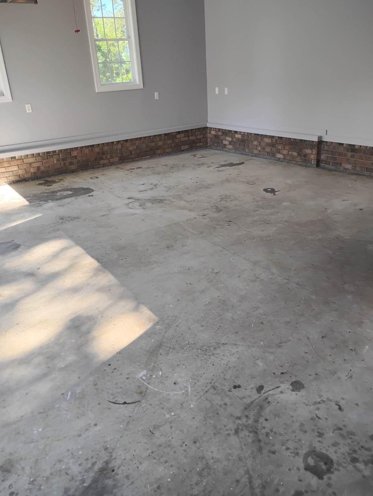 Empty unfinished room with gray concrete floor, white walls, a small window, and brick trim along the baseboards.
