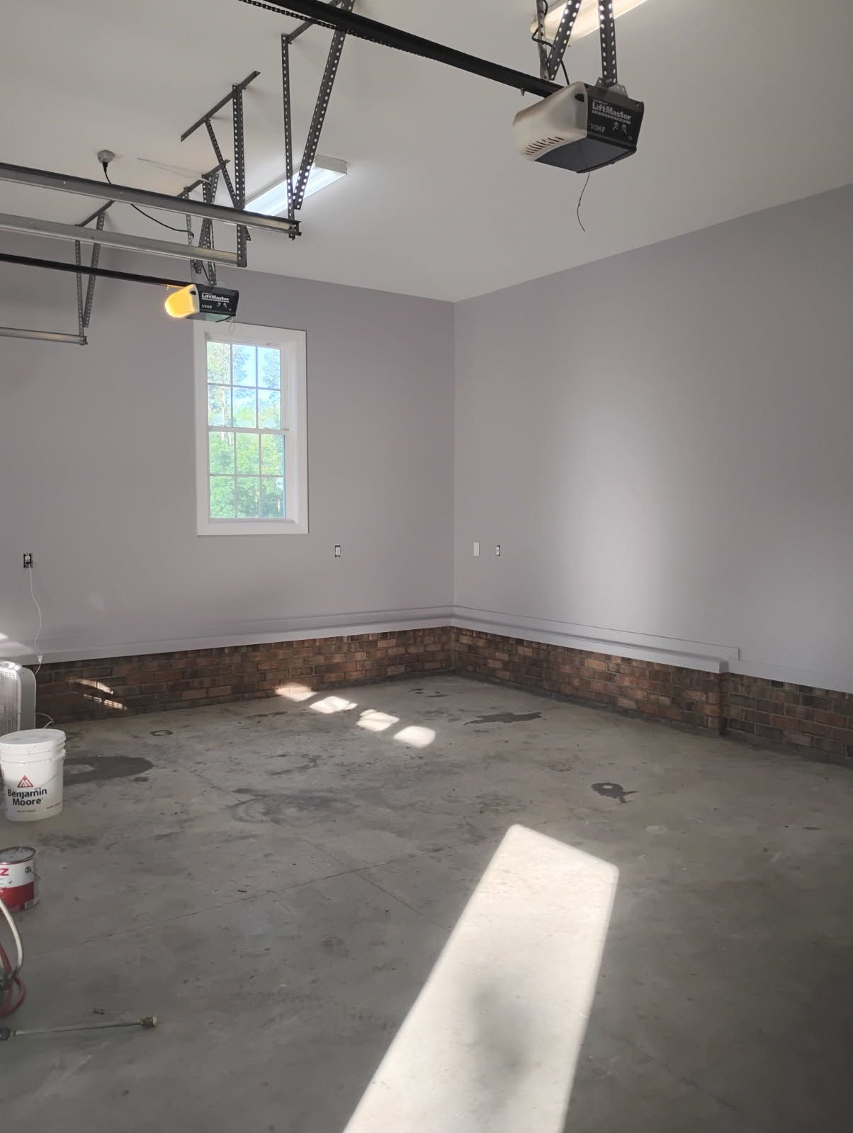 Empty garage with gray walls, concrete floor, and sunlight streaming through a small window.