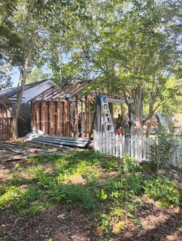Damaged wooden shed with collapsed roof and white picket fence in a shaded backyard