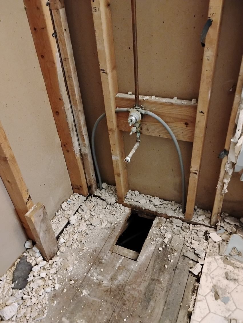 Damaged bathroom floor with exposed framing, plumbing pipe, and a hole in the subfloor