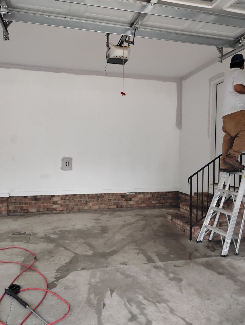 Empty garage with unfinished brick wall, concrete floor, ceiling opener, and a ladder by the stairs.