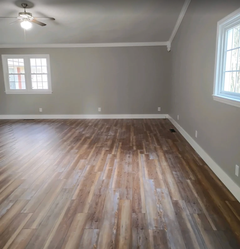 Empty living room with gray walls, wood-look flooring, ceiling fan, and windows on two sides