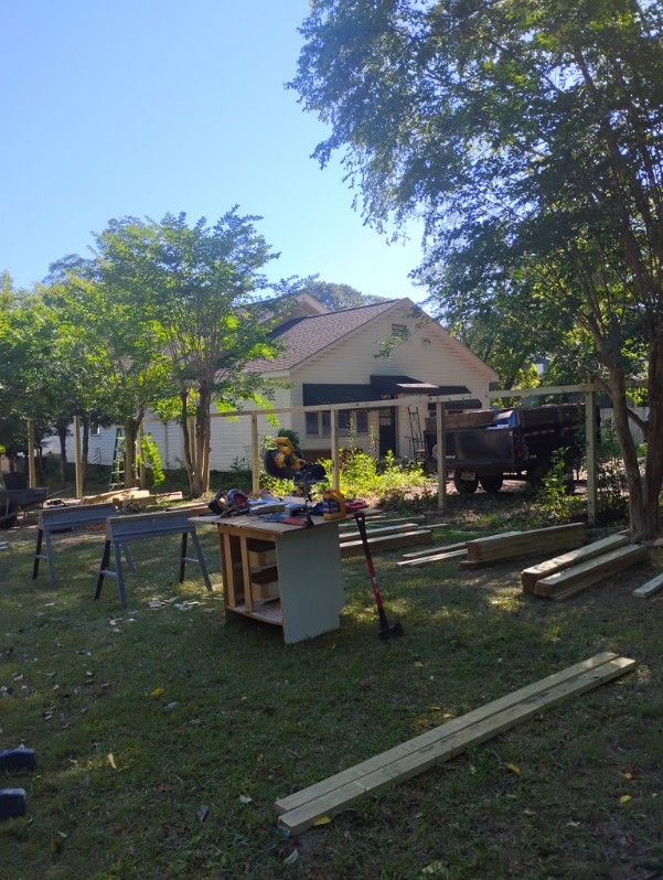 Backyard with house, trees, workbench, and lumber scattered across the grass