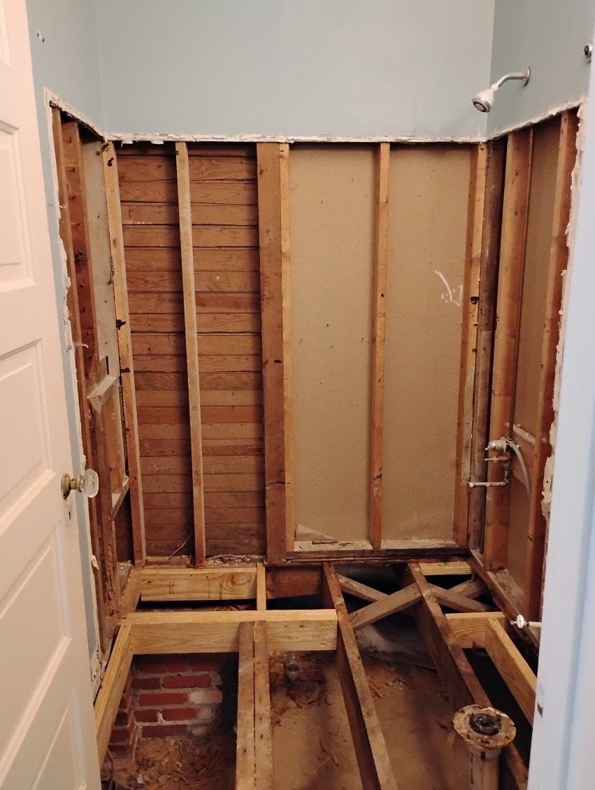 Bathroom wall studs exposed during demolition, with removed drywall and floor framing visible.