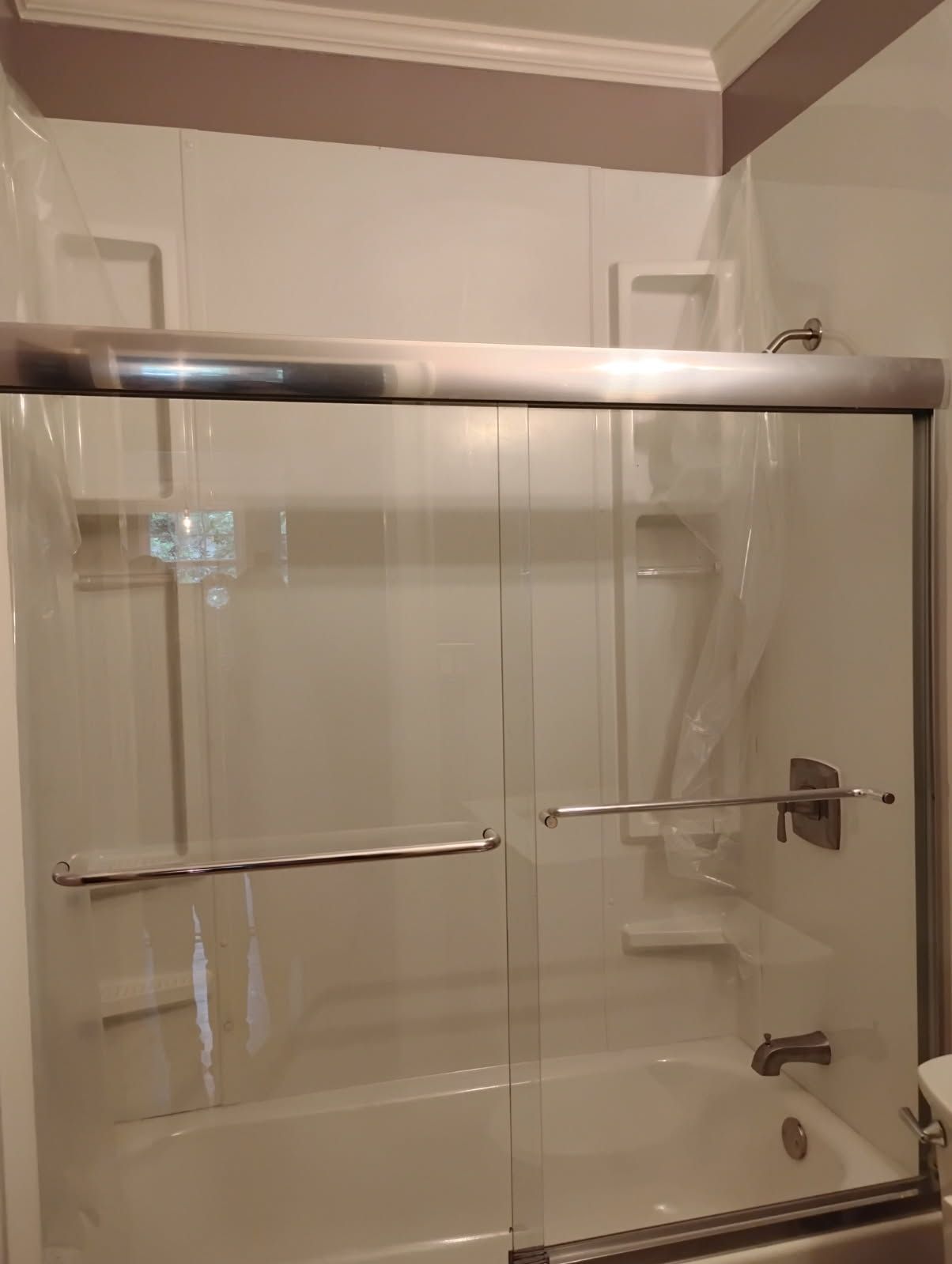 Bathroom shower with clear sliding glass doors, chrome bars, and beige tile walls.