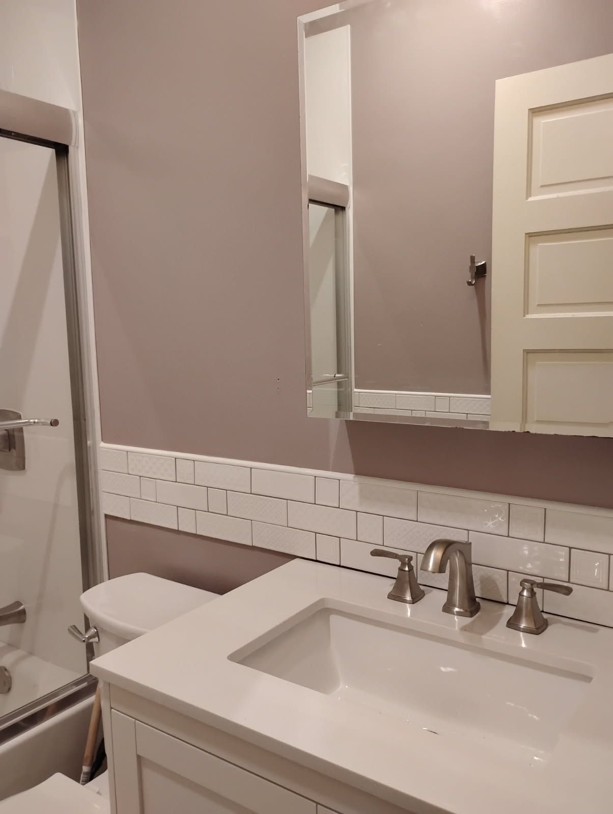 Small bathroom with white vanity, mirror, tiled backsplash, and shower door.