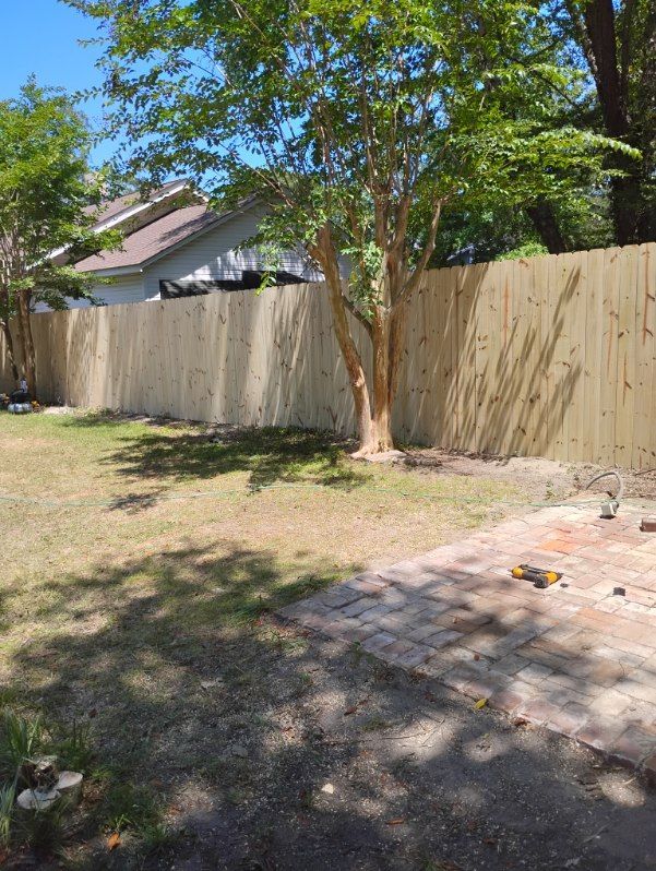 Backyard with a tree, wooden fence, and stone patio in bright sunlight