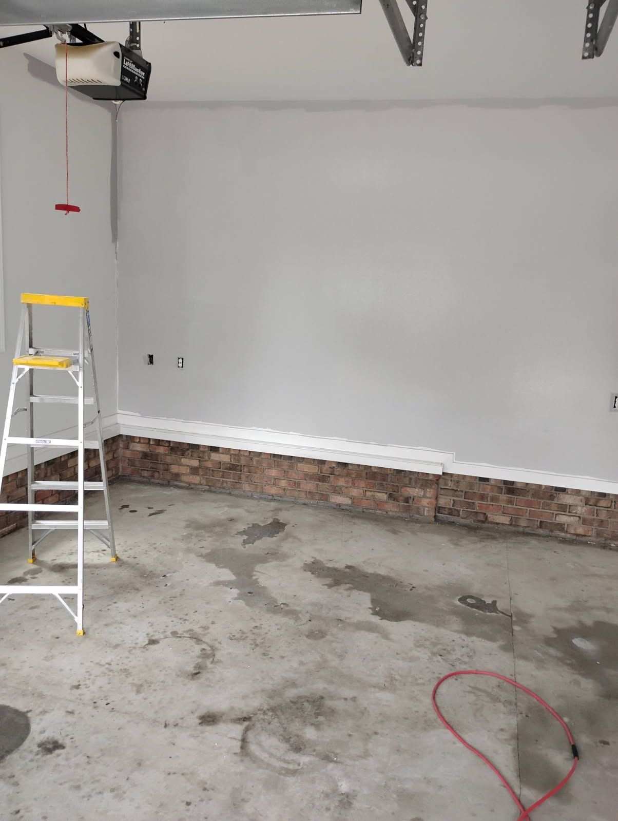 Empty garage interior with gray walls, concrete floor, ladder, and exposed garage door track